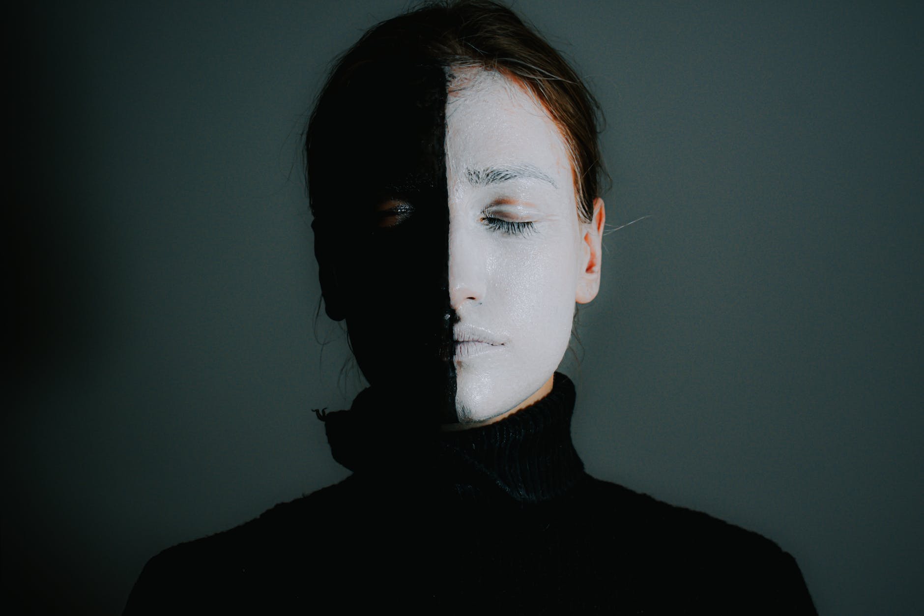 female with face painted in black and white standing with closed eyes