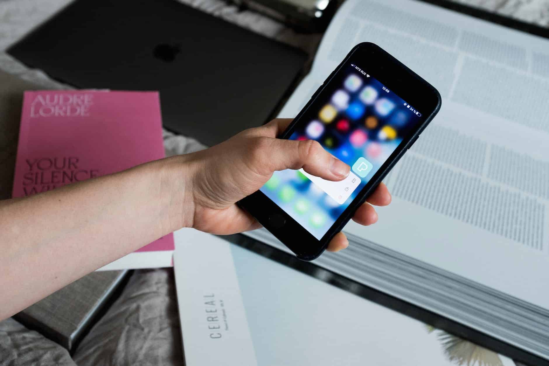 crop unrecognizable person touching smartphone screen and having open encyclopedia